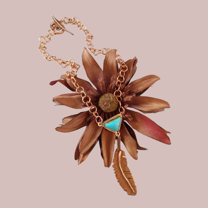 Handmade custom feather necklace with turquoise cabochon displayed on a brown flower, hand crafted by SoufiiArte Studio.