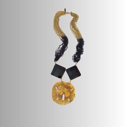 Handcrafted brass sand dollar necklace with black faceted onyx and black-gold multi-strand chains part of the SOUFiiARTe Resort Collection.